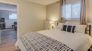 A bedroom with a large bed, a desk with a chair, and a window with curtains. - Westside Value Parks & Trails Close to it all (Colorado Springs)