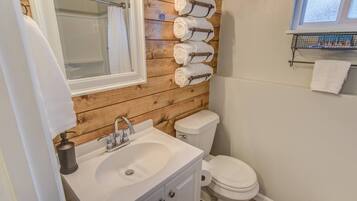 A bathroom with a wooden wall, a sink, a toilet, and a towel rack with multiple towels.