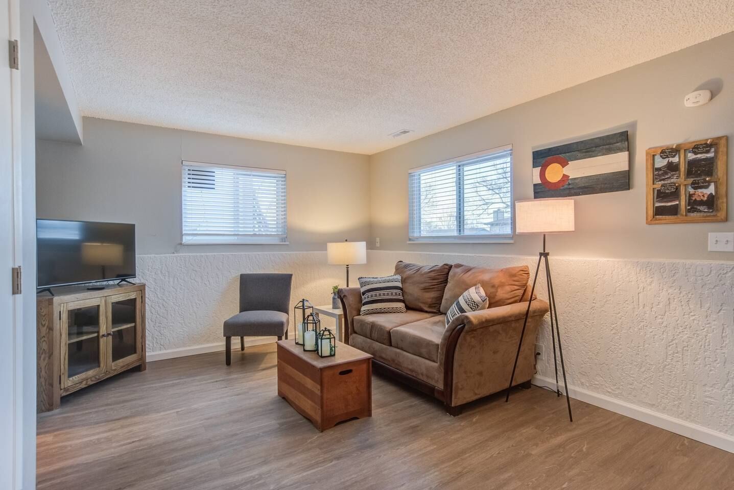 A living room with a TV, wooden cabinet, couch, chair, and floor lamp.