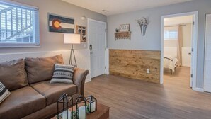 A cozy living room with a brown leather sofa, a wooden accent wall, and a door leading to a bedroom. - Westside Value Parks & Trails Close to it all (Colorado Springs)