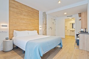 A modern hotel room with a large bed, a wooden accent wall, a small round side table, and a kitchenette area. - Colectia Hotel Ondarreta (San Sebastián)