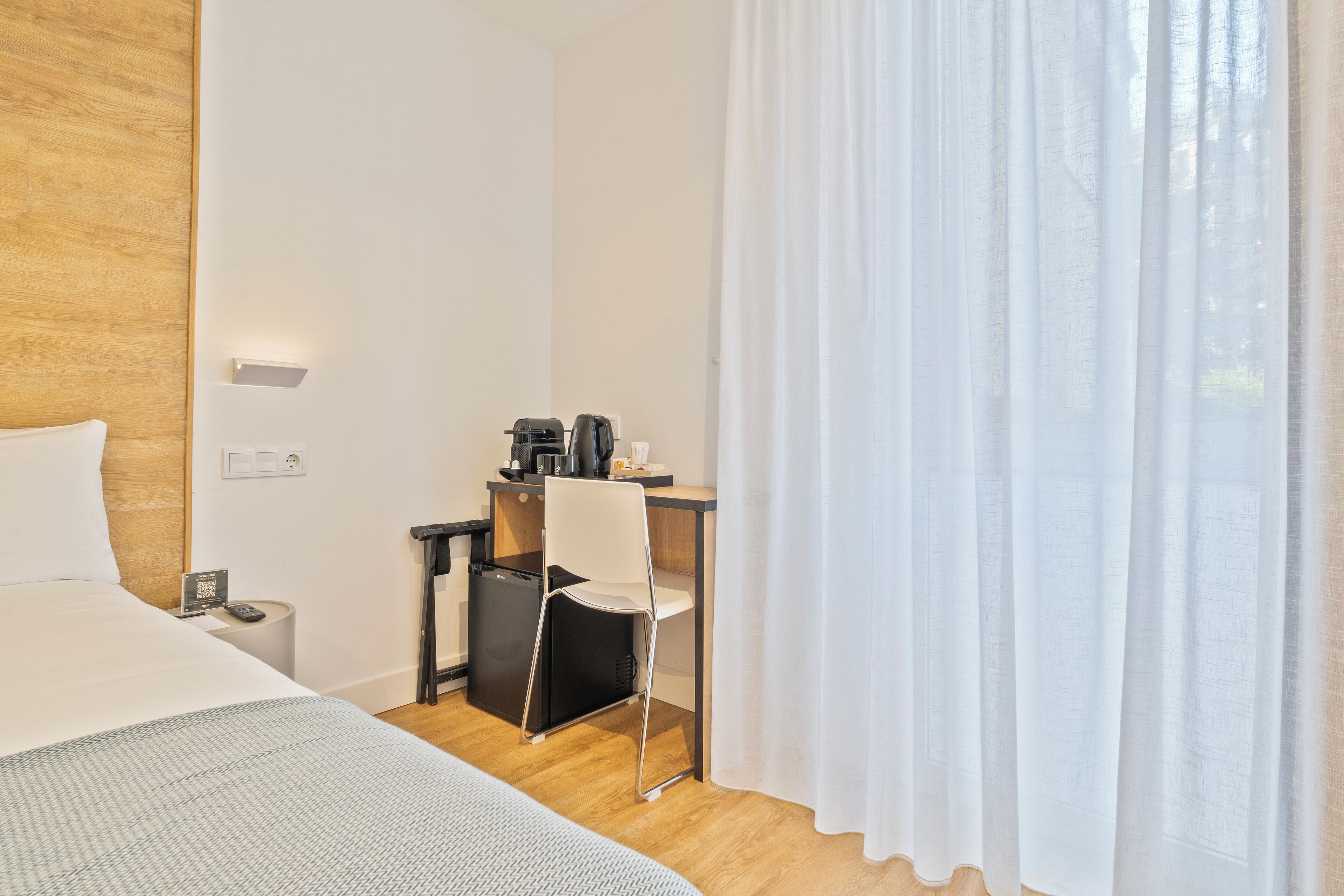 Een hotelkamer met een bed, een bureau met stoel, een koffieapparaat en een kleine koelkast.