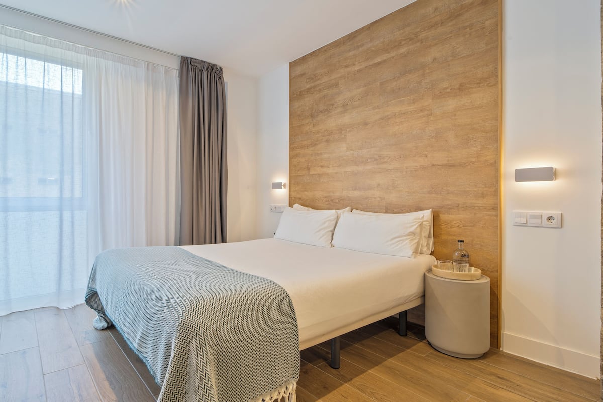 Quarto de hotel moderno com uma cama grande, uma mesa de cabeceira, um criado-mudo redondo e uma parede de destaque em madeira.
