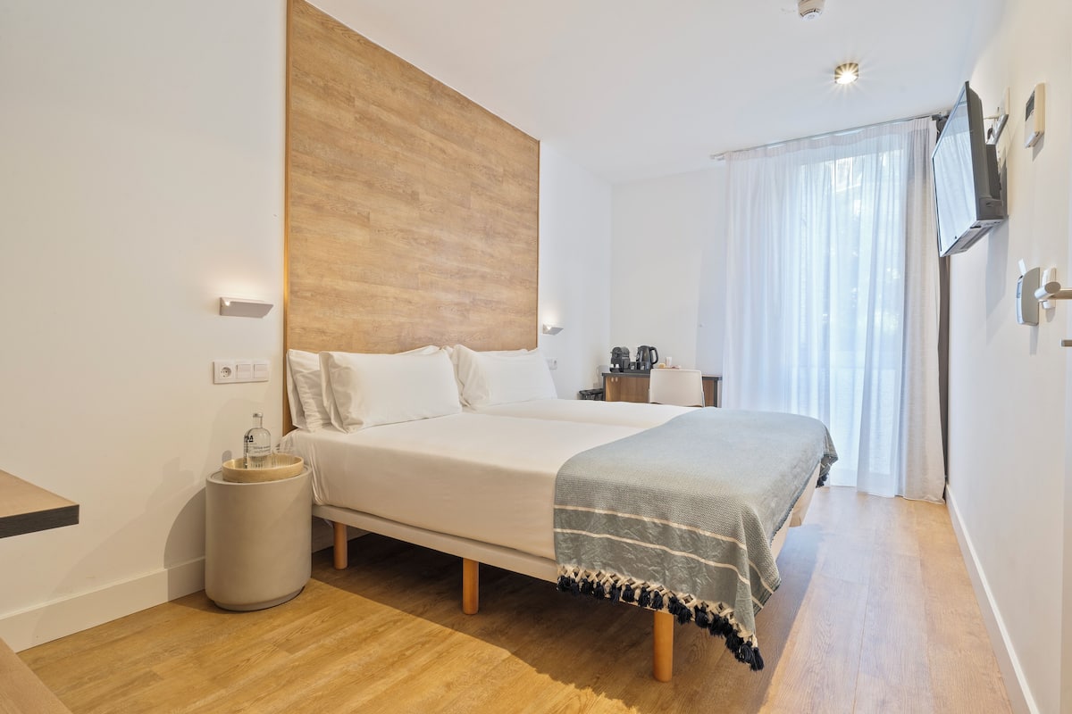 Quarto moderno com cama grande, cabeceira de madeira, mesa de cabeceira e televisão na parede.