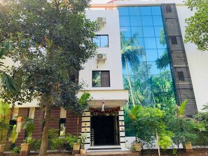 Un edificio moderno con fachada de vidrio, una entrada tradicional con arco decorativo y un jardín circundante con diversas plantas.