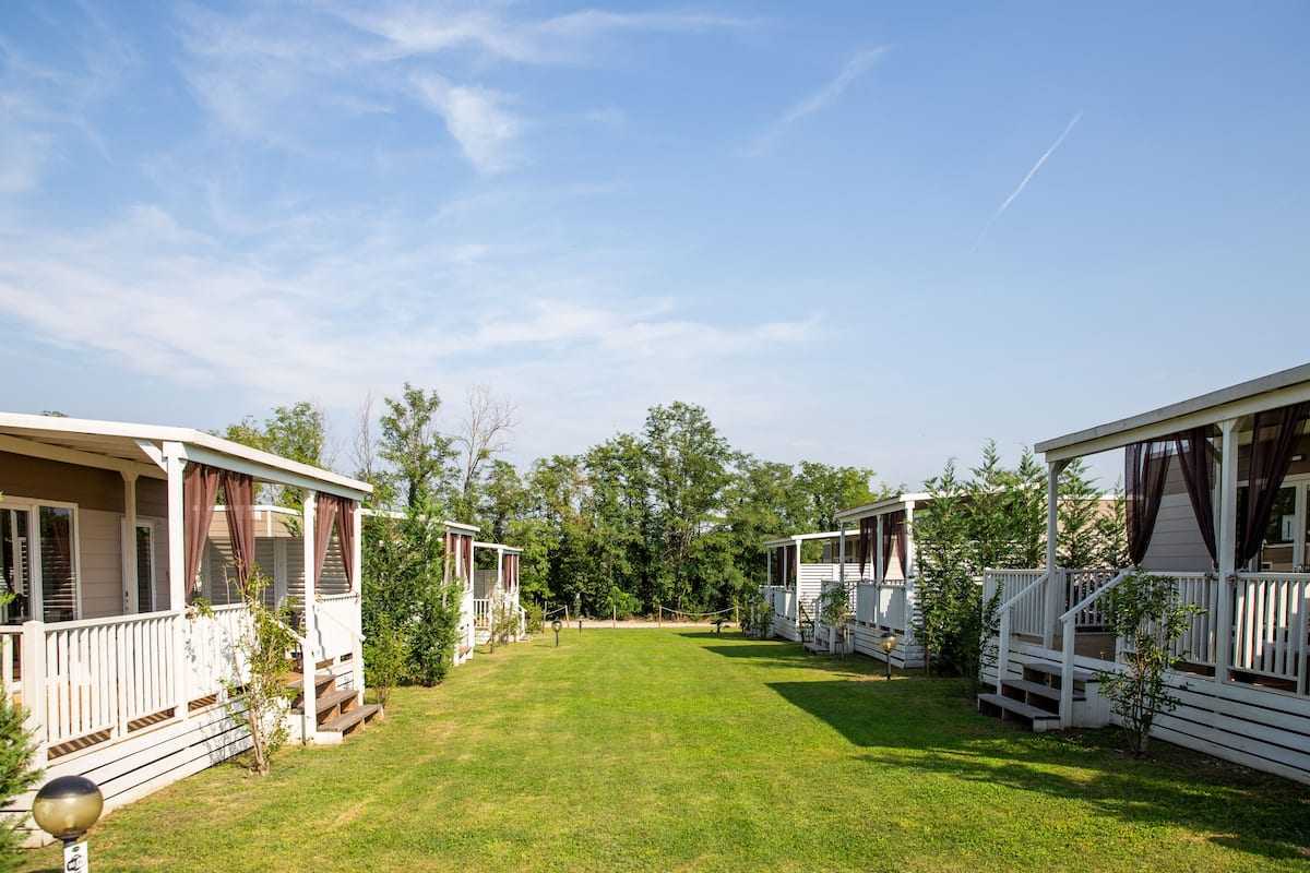 A row of mobile homes with a grassy yard and trees in the background.