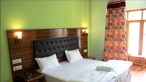 A neatly made bed with a wooden headboard, two bedside tables, and a nightstand with a phone. - TIH Jeevanam Villa - Leh (Leh)