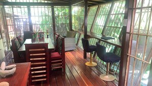 A covered outdoor seating area with wooden tables and chairs, a small rug, and a stone sculpture. - Zen Villa # 1 -  Three bedroom Luxury Villa with Private Garden -Playa Chiquita (Puerto Viejo de Talamanca)