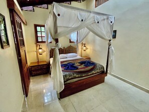 A four-poster bed with a canopy, two bedside lamps, a patterned bedspread, and a wooden headboard.