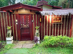 A wooden structure with a red door, a sign reading 'ZEN VILLA #1', and potted plants.