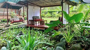 A covered outdoor seating area with a table and chairs, surrounded by lush greenery and a pond. - Zen Villa # 1 -  Three bedroom Luxury Villa with Private Garden -Playa Chiquita (Puerto Viejo de Talamanca)