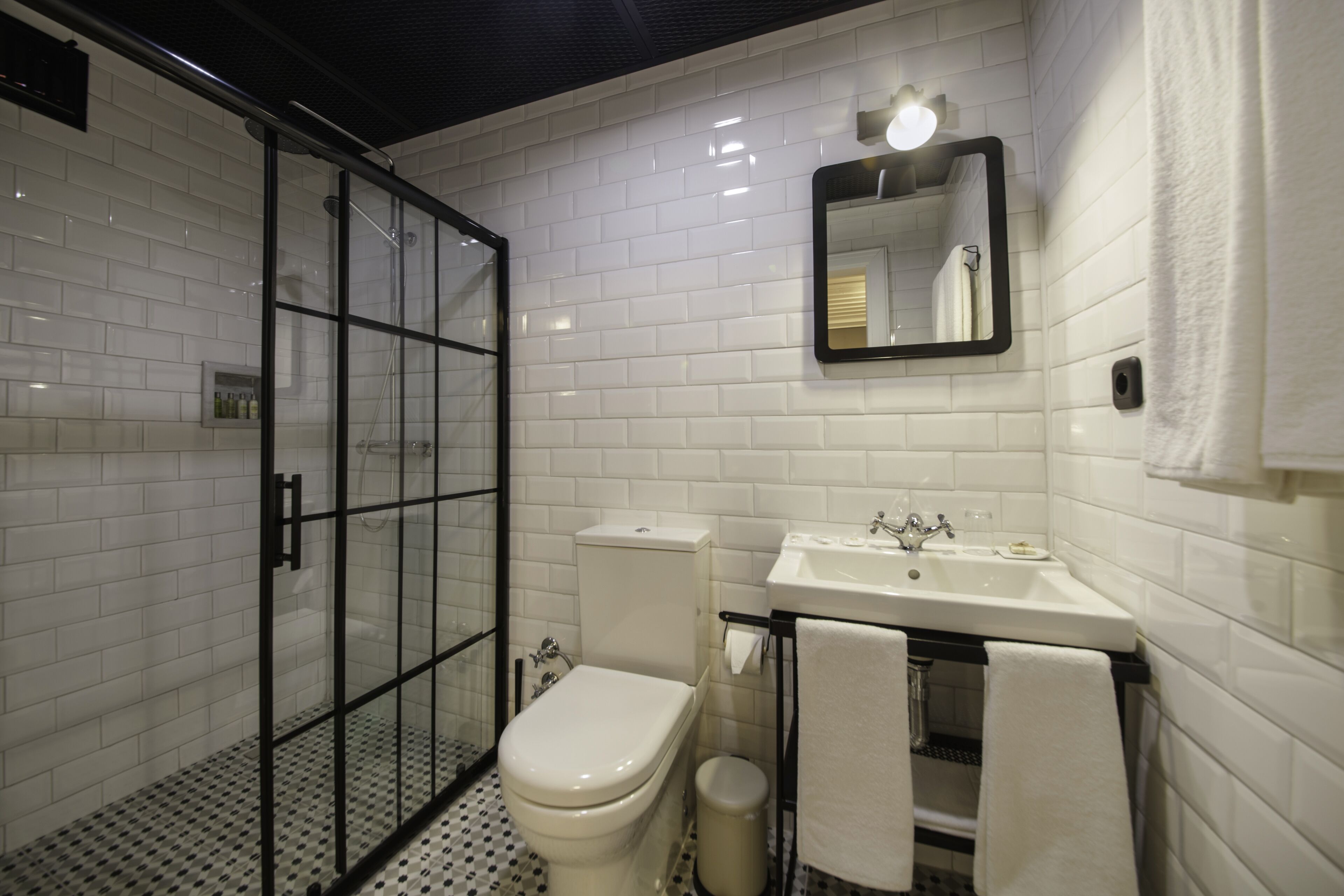 Ein modernes Badezimmer mit weißen Subway-Fliesen, einer gläsernen Dusche, einer weißen Toilette, einem Waschbecken mit Spiegel darüber und einem Handtuchhalter.