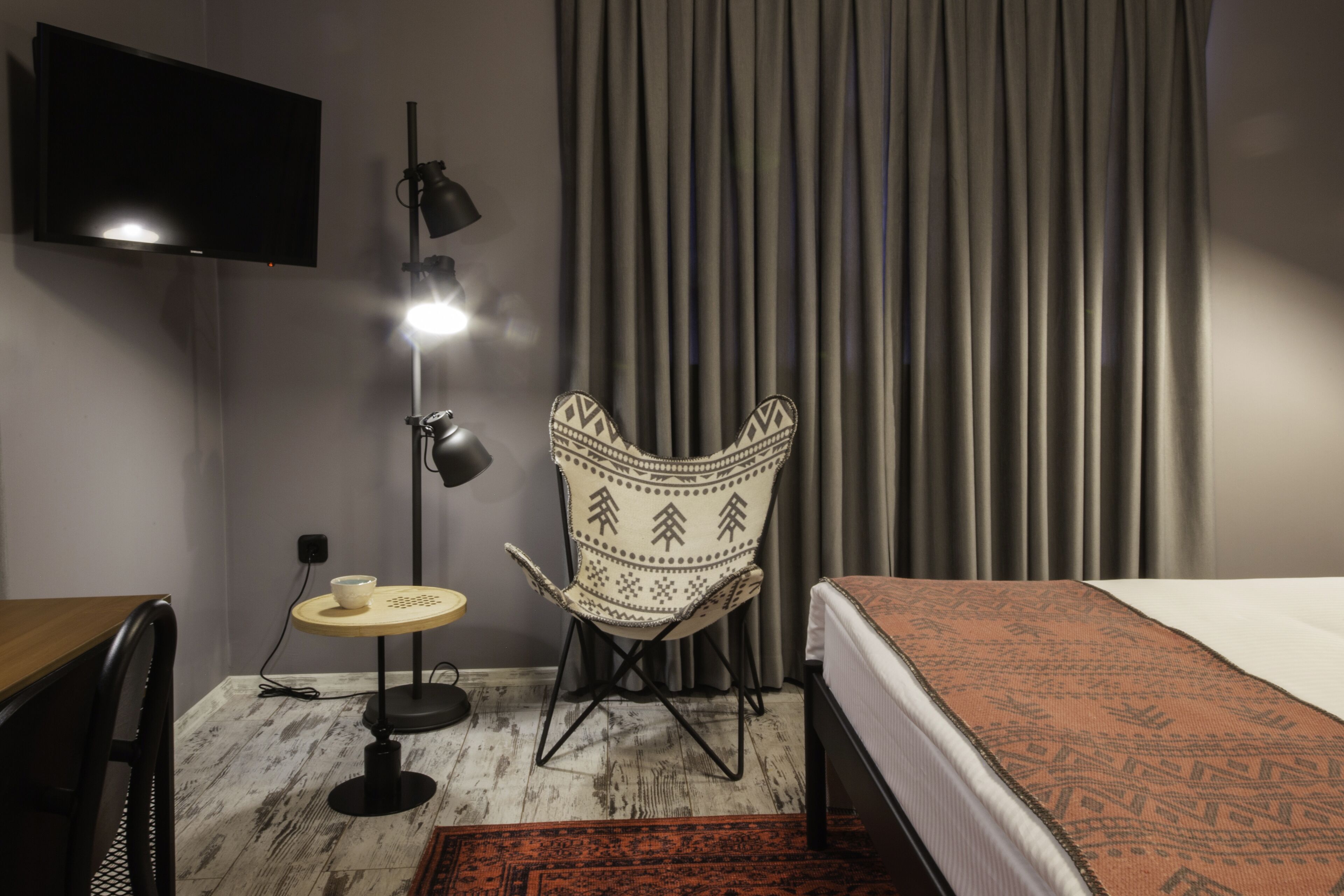 Una habitación de hotel con una cama, una silla, un escritorio, una lámpara y un televisor.