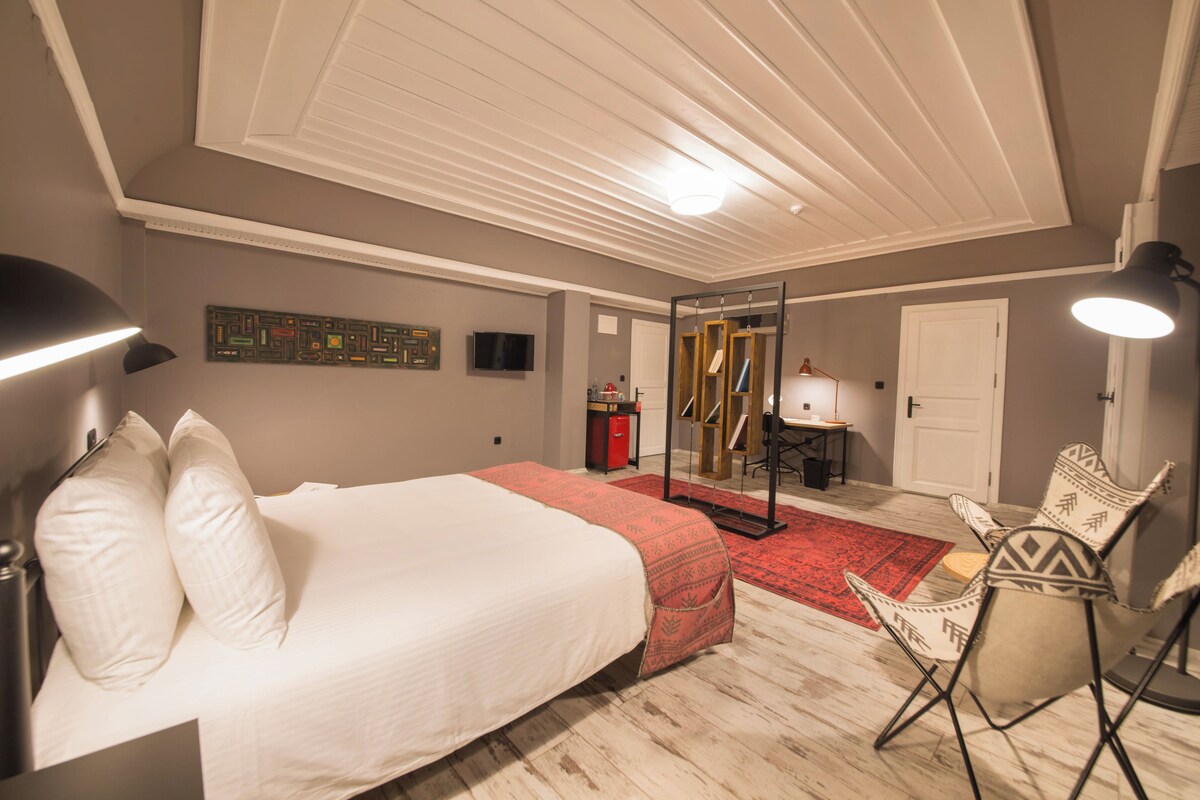 A bedroom with a large bed, a desk, a chair, a TV, and a red rug.