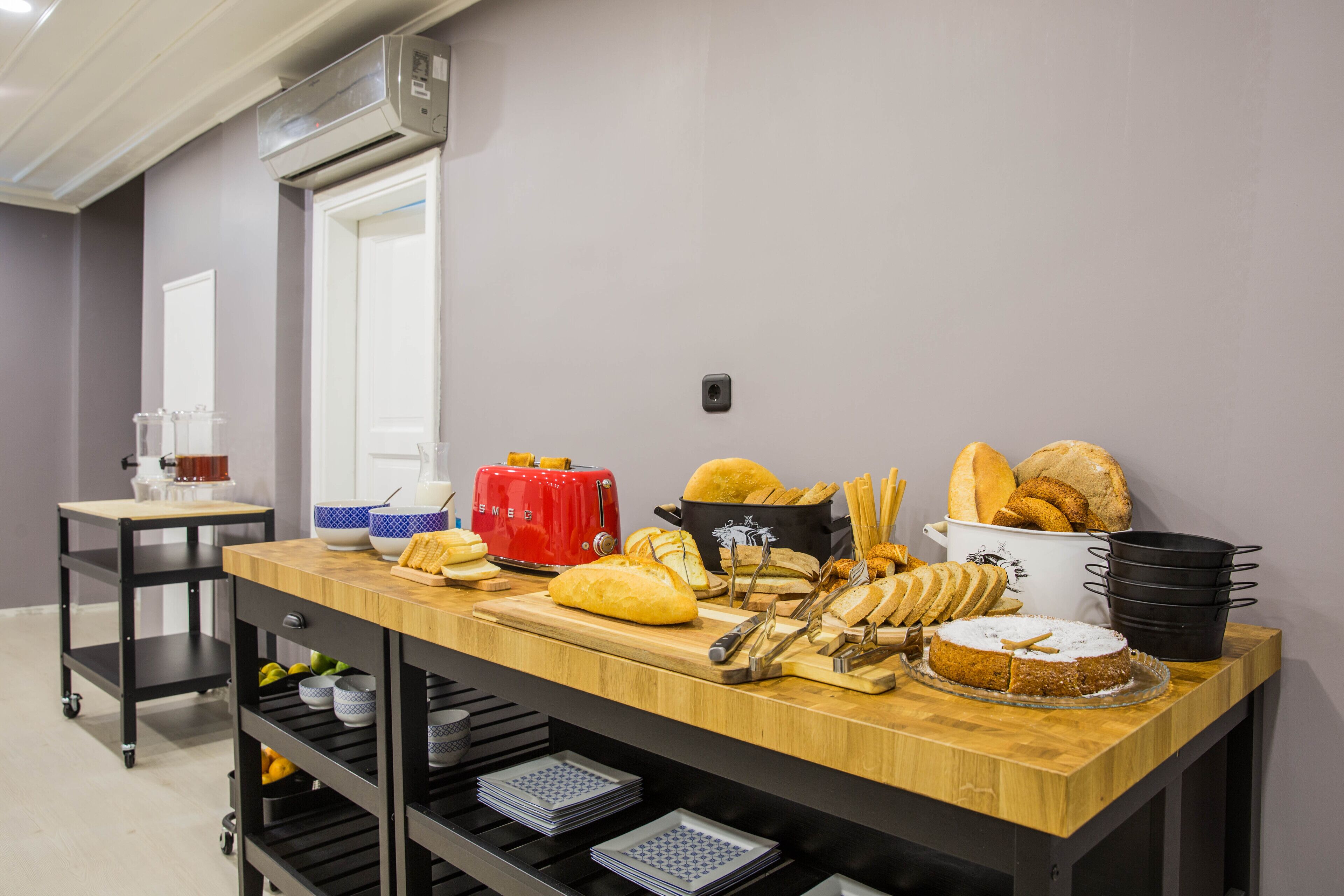 A buffet setup with various breads, a red toaster, and a cake on a wooden counter.