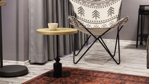 A modern room with a patterned armchair, a small round table with a cup, and a black floor lamp.