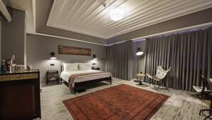A modern hotel room with a large bed, a small desk, a chair, a rug, and a curtain-covered window.