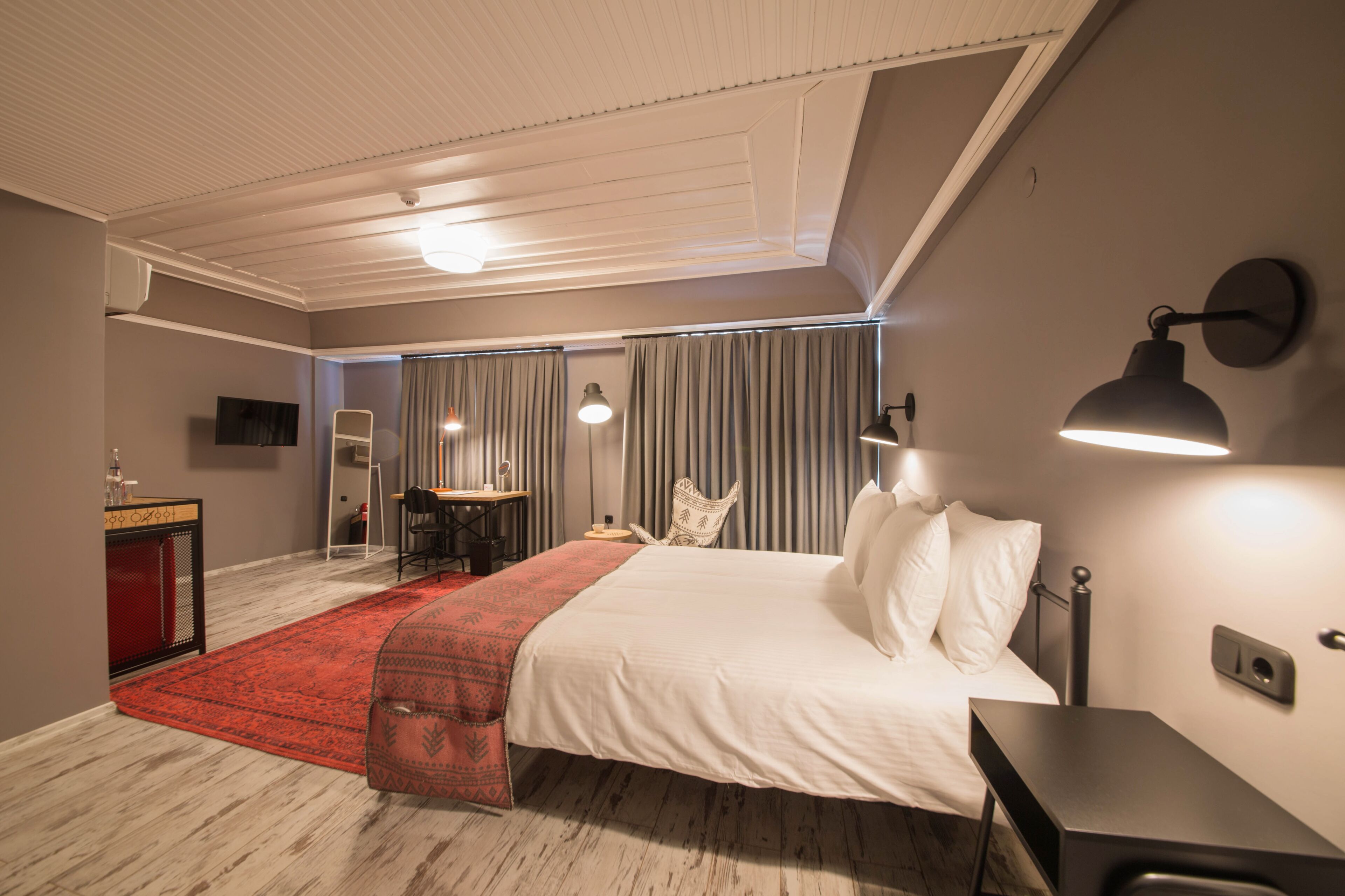A hotel room with a bed, bedside table, lamp, and a desk with a chair.