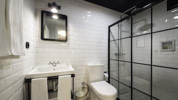 Un baño moderno con azulejos blancos tipo metro, una ducha con mampara de vidrio, un lavamanos blanco y un inodoro.
