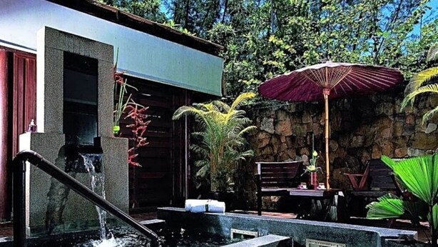 A pool area with a stone wall, a wooden deck, and a stone structure with a water feature.