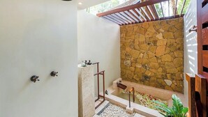A shower with a stone wall, a wooden bench, and a small pool.