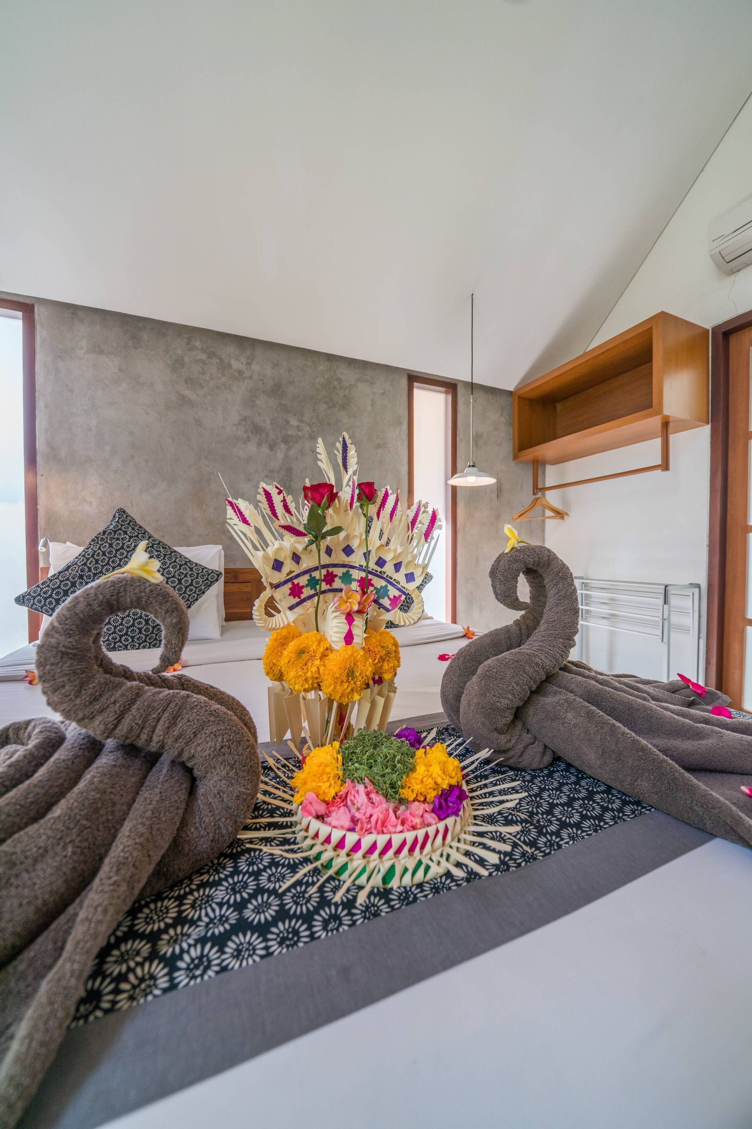 A modern hotel room with a large bed, a decorative swan-shaped towel, a colorful flower arrangement, and a minimalist design.