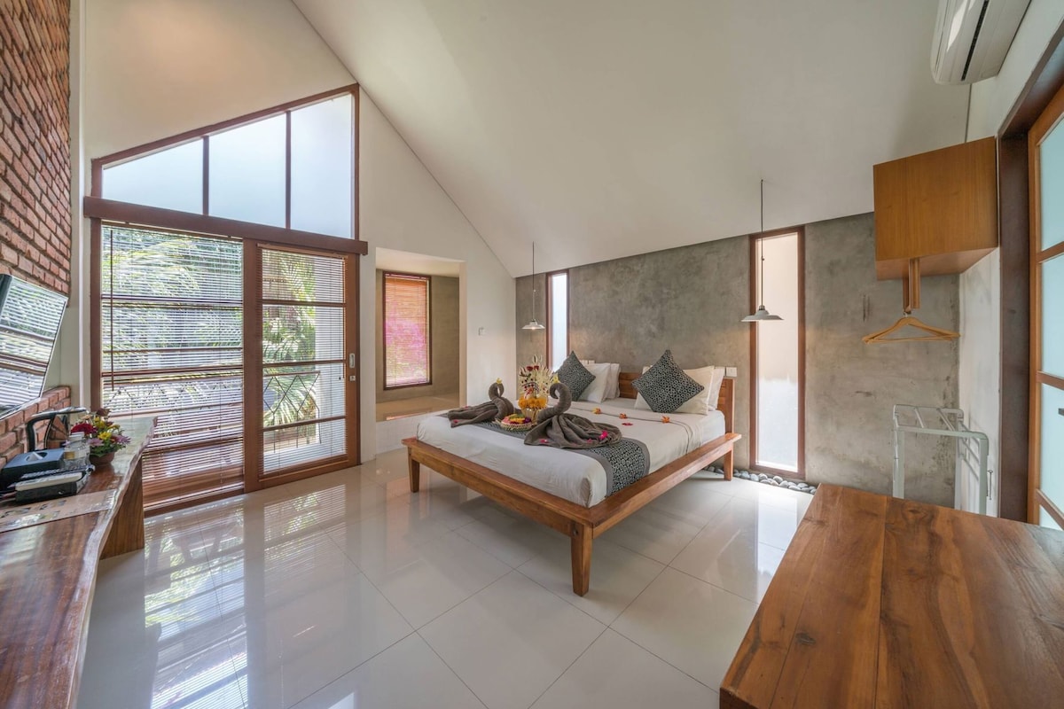 A modern bedroom with a large bed, a wooden desk, and a view of the outdoors.