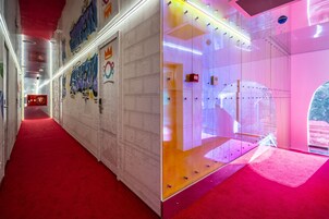 Un pasillo con alfombra roja, grafitis en las paredes y un ascensor de vidrio con iluminación rosada.
