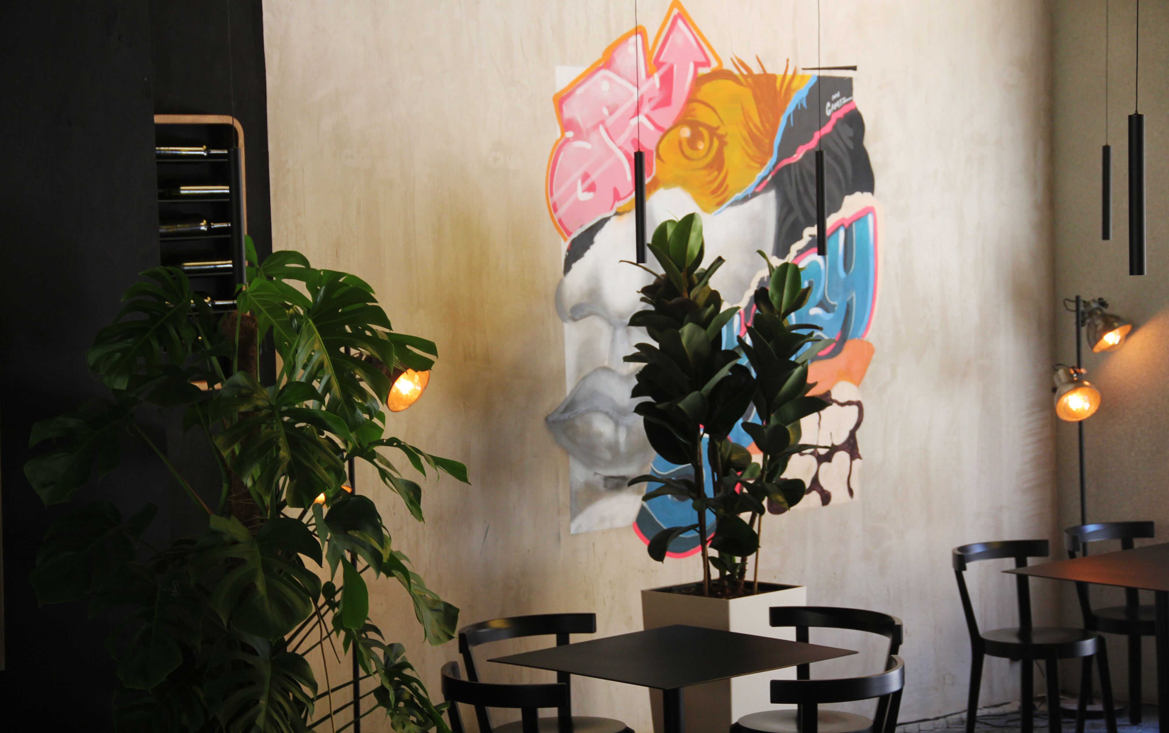 A restaurant interior with a mural, potted plants, and a table with chairs.