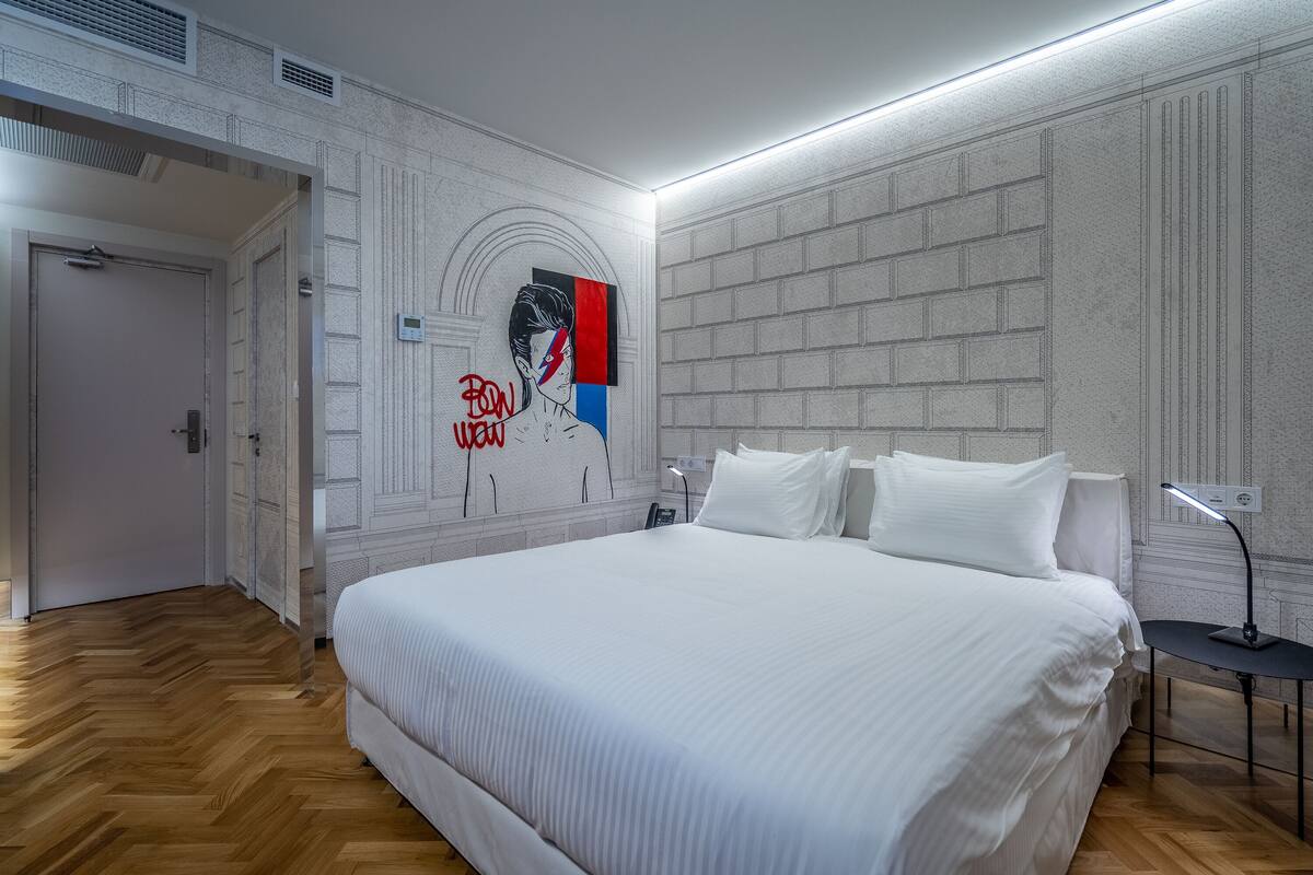 A hotel room with a large bed, a wall mural, and a modern design.