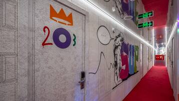 Un pasillo con alfombra roja, una puerta con el número 203 y un símbolo de corona, y una pared con grafitis coloridos y un bocadillo de diálogo.