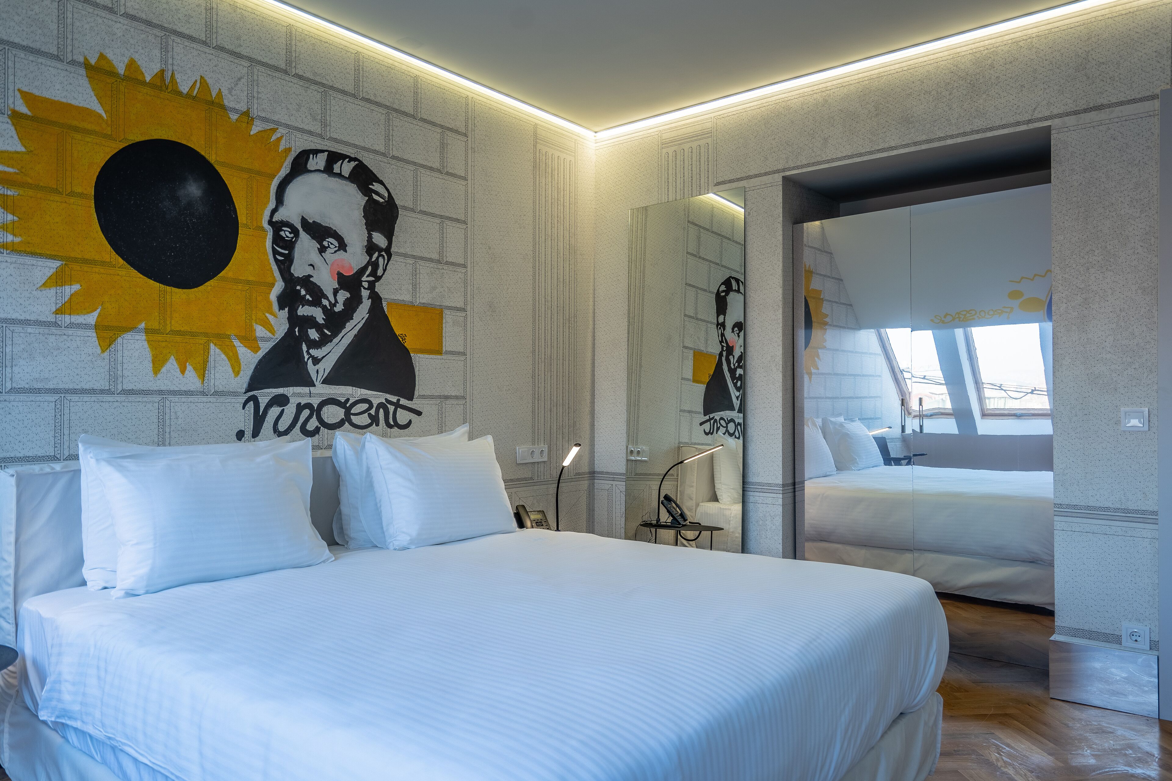 A modern hotel room with a large bed, a mirror, and a wall mural.