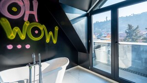 Un baño moderno con una bañera independiente, un ventanal con vista a la ciudad y una pared con grafitis de colores.