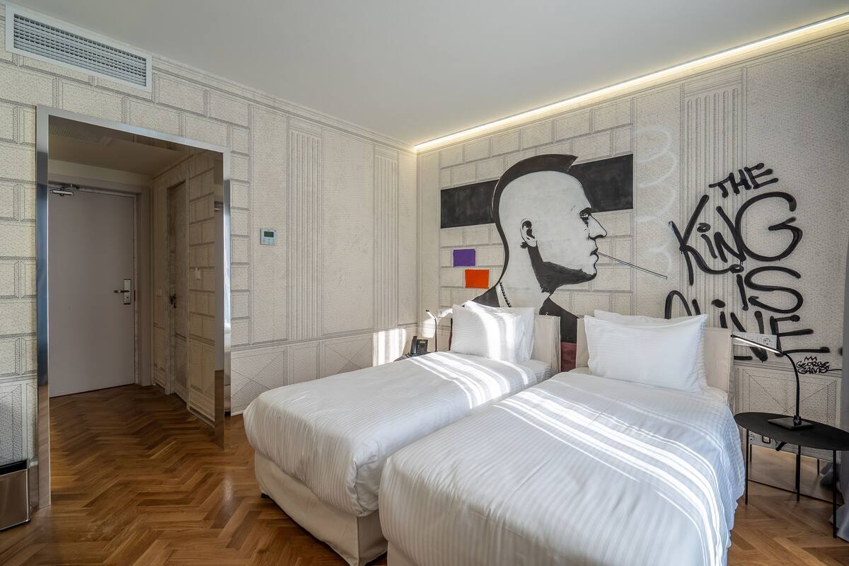 A hotel room with two beds, a mural on the wall, and a modern design.