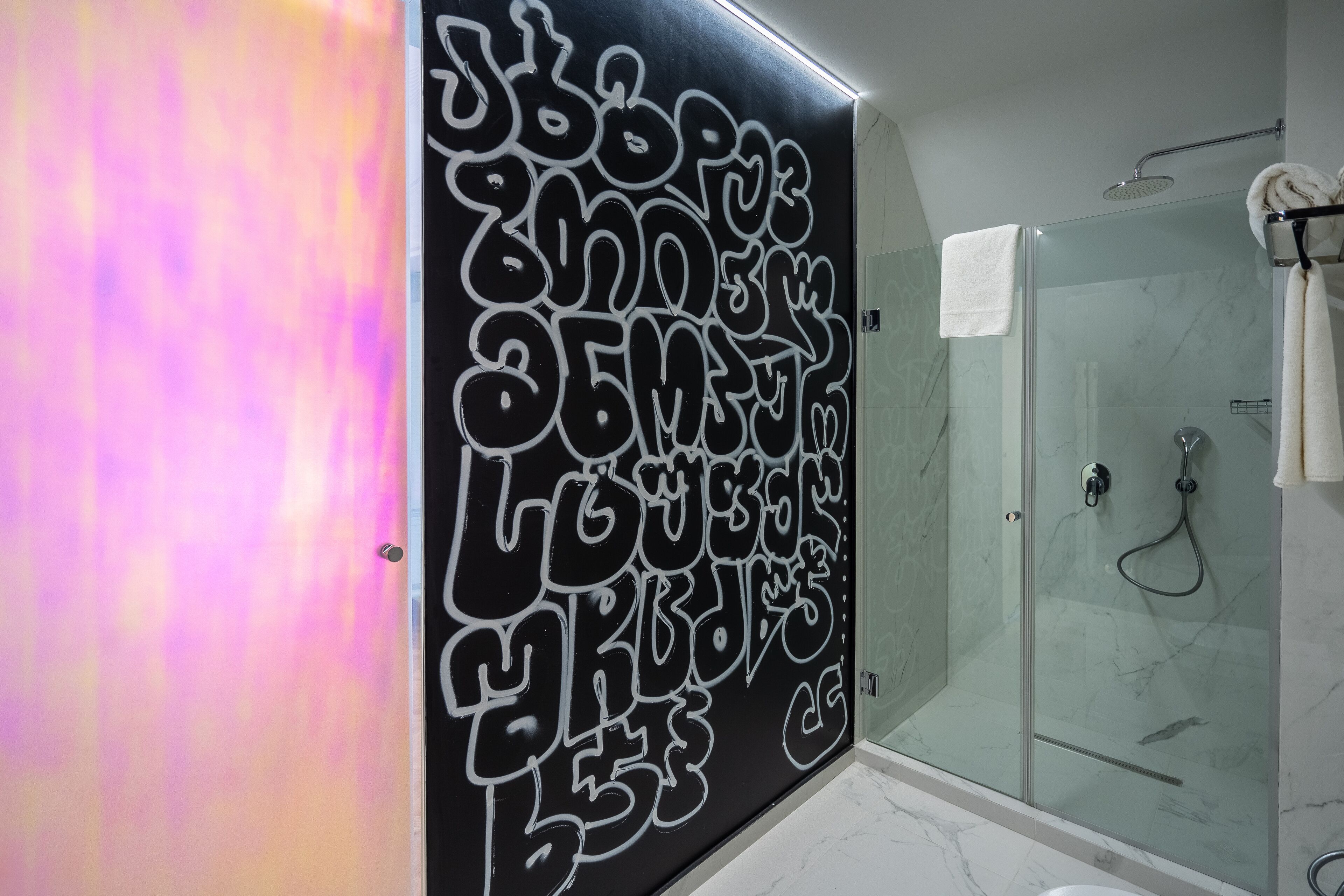 A bathroom with a glass shower enclosure, a marble-tiled floor, and a wall with graffiti-style text.