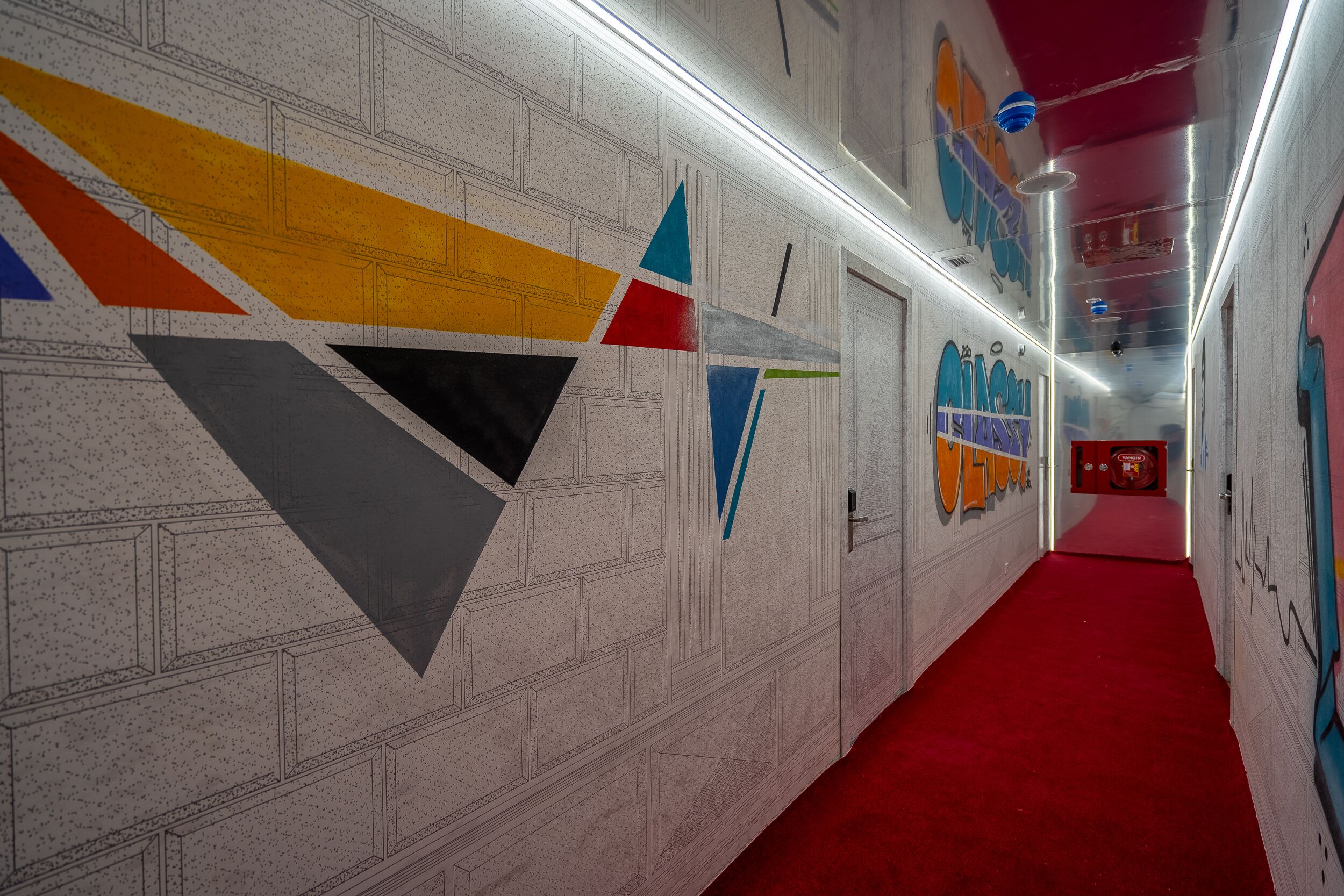 A hallway with geometric wall art, a red carpet, and a red ceiling.