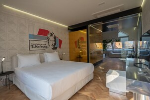 A modern bedroom with a large bed, a glass partition, and a view of a living area.