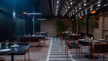 A restaurant with tables and chairs, a brick wall, and hanging lights.