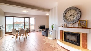 A spacious living room with a fireplace, a large wall clock, and a dining area with chairs and a table. - Victus Apartamenty - Cadena 1 (Sopot)