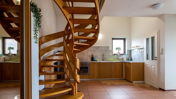 A modern kitchen with a wooden spiral staircase, wooden cabinets, and a tiled floor. - Victus Apartamenty - Cadena 1 (Sopot)