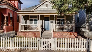 A two-story house with a front porch, a mailbox, and a white picket fence.