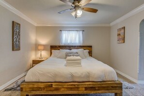 A bedroom with a wooden bed frame, a ceiling fan, a bedside lamp, and a window with sheer curtains.