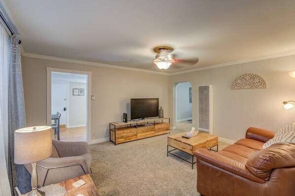 A living room with a TV, leather sofa, and a ceiling fan.