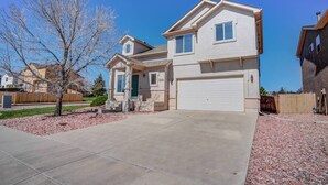 A two-story house with a front garage, a covered porch, and a well-maintained lawn. - 3BR AF Academy Pet-friendly (Colorado Springs)