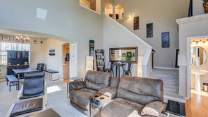 A spacious living room with a large leather sofa, a dining area with a table and chairs, a kitchen in the background, and a staircase leading to an upper level. - 3BR AF Academy Pet-friendly (Colorado Springs)
