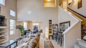 A spacious living room with a large sofa, a dining area, and a staircase leading to an upper floor. - 3BR AF Academy Pet-friendly (Colorado Springs)
