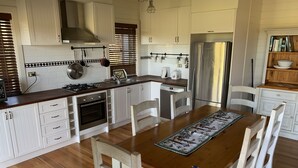 A modern kitchen with white cabinetry, a stainless steel refrigerator, and a wooden dining table with chairs. - Peppergrove Cottage (Berry)