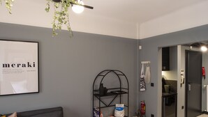 Ein modernes Wohnzimmer mit einem grauen Sofa, einem roten Hocker, einem schwarzen Tisch mit einem Buch und einer schwarzen Regaleinheit mit Zeitschriften und einer Pixel Tasche.