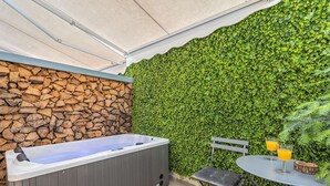 A hot tub, a table with drinks, and a stone wall with greenery. - Blue Mountain Guesthouse "Freya” (Arachova)