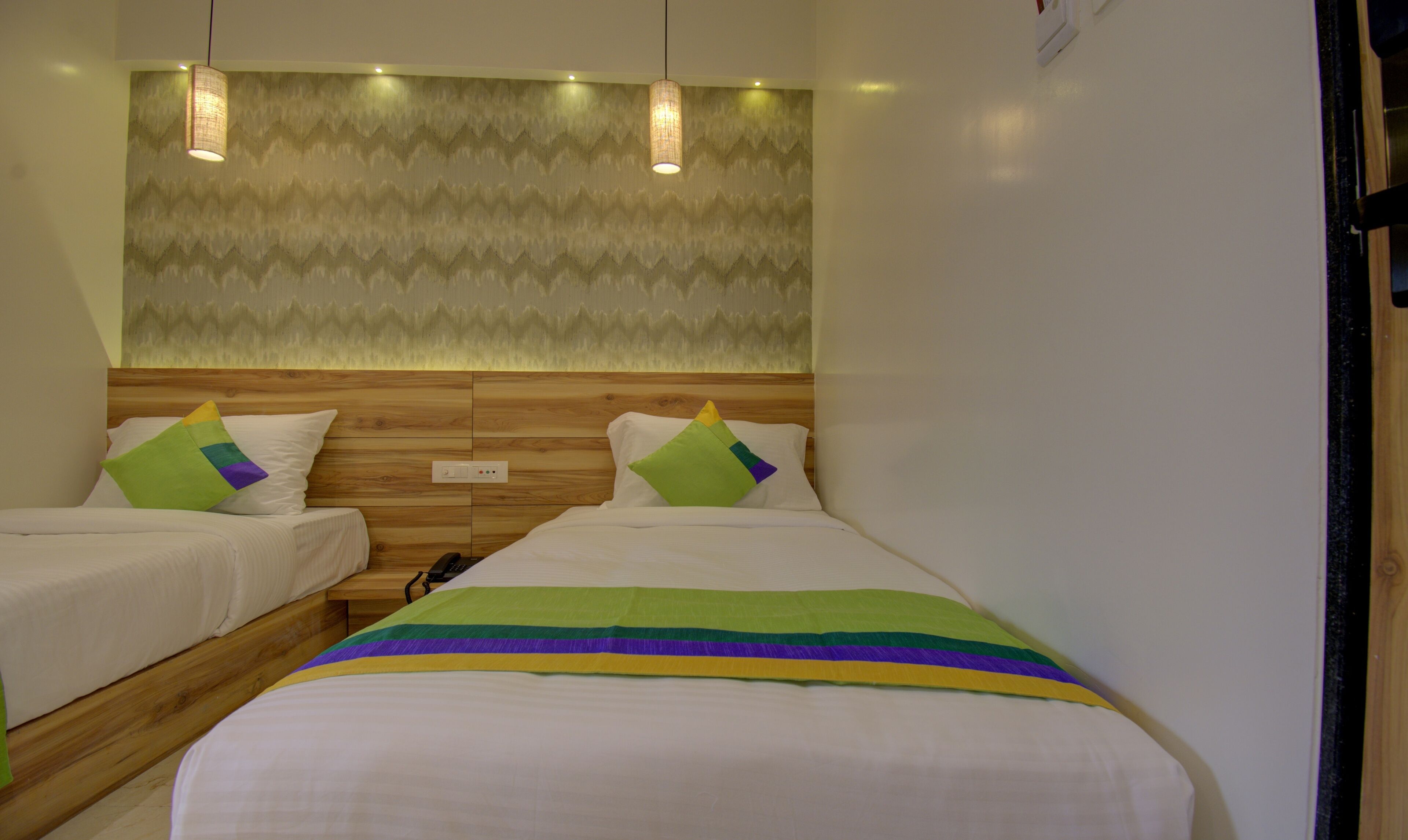 A hotel room with two single beds, a wooden headboard, and a patterned wall.